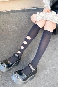 Détail de chaussettes hautes noires avec découpes latérales et chaussures Mary Jane