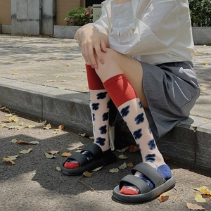 Detail of sheer JK socks with blue patterns and red ribbed cuffs worn with sandals