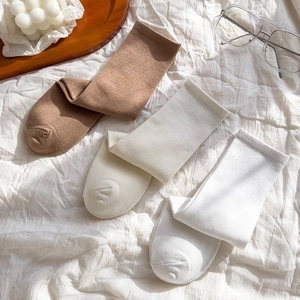 Three pairs of mid-calf cotton socks in neutral tones displayed on cozy white bedding
