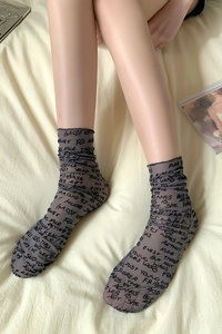 Close-up of sheer grey calf socks with black letter print and delicate ruffled edges
