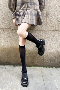 Close-up of black knee-high socks with diamond pattern and patent leather Mary Jane shoes