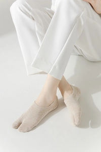 Detail of low-cut two-toe socks in beige knit, shown with white casual pants