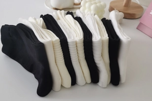 Detail of ribbed crew socks in black and off-white stacked in a minimalist home setting