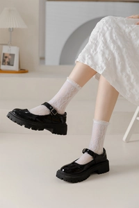 Detail of white lace patterned calf socks styled with black platform Mary Jane shoes