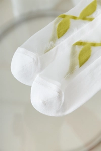 Macro detail of sheer white floral socks with delicate green leaf embroidery patterns