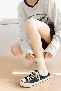 Detail of white ribbed velvet crew socks worn with black canvas sneakers on wood floor