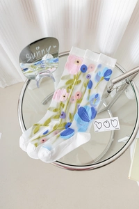 Detailed view of three sheer mesh calf socks with floral embroidery on glass table