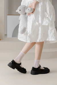 Close-up of white lace mesh socks paired with black patent leather Mary Jane shoes