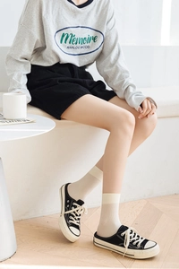 Close-up of stylish off-white crew socks paired with black shorts and canvas sneakers