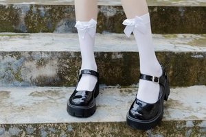 Close-up of JK style white knee-high socks with satin bows and black Mary Jane shoes