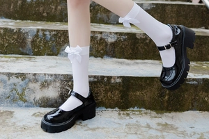 Detail of black patent leather platform Mary Janes with white bow knee-high socks