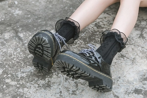 Close-up of black patent leather platform shoes with iconic yellow stitching and lace socks