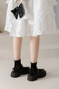 Detail of black patent leather platform Mary Jane shoes with lace mesh socks and bow bag