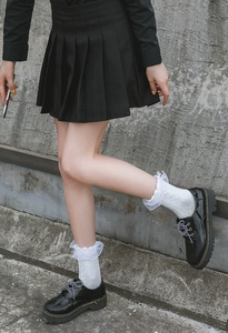 Detail of white lace ruffle socks paired with black pleated skirt and chunky leather shoes