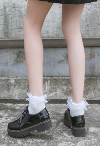 Detail of black platform loafers with yellow stitching and white ruffled lace socks