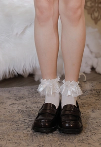 Dettaglio di calze Lolita bianche con pizzo e fiocchi di raso abbinate a scarpe marroni