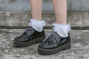 Detail of black patent leather platform shoes with yellow stitching and white lace socks