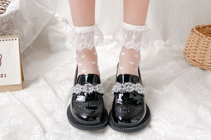 Détail de chaussettes en dentelle blanche avec broderie cœur et mocassins noirs vernis