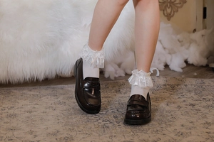 Dettaglio di calze Lolita in pizzo bianco con fiocchi di seta e bordi a balze con mocassini