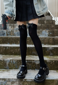Detailed close-up of black velvet over-knee high socks with satin bow accents