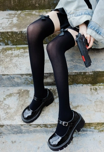 Close-up of black over-knee high socks with satin bows and platform Mary Jane shoes