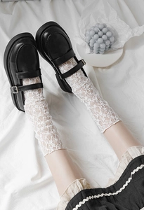 Detail of white lace mesh socks paired with black platform Mary Jane shoes and buckles