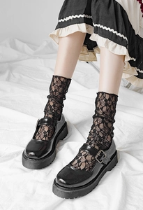 Close-up of black Mary Jane shoes with floral lace crew socks and pleated skirt