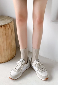 Detail of beige ribbed crew socks paired with white sneakers on a wooden background