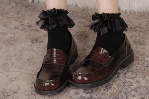 Dettaglio di pizzo Lolita e fiocco su calze abbinate a mocassini vintage in stile collegio