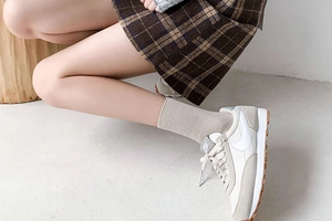 Detail of retro sneakers paired with white mid-calf socks and a brown plaid pleated skirt