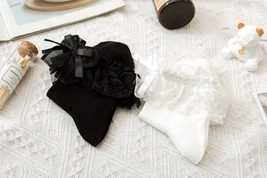 Dettaglio di calze Lolita con pizzo e fiocchi decorativi su una base in maglia bianca
