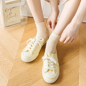 Pale yellow canvas sneakers paired with breathable beige mesh frill socks on wood floor
