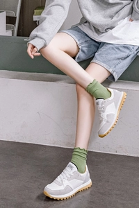 Detail of green frilly edge striped split-toe socks worn with retro patchwork sneakers