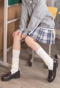 Detail view of white knitted leg warmers with grey zip hoodie and plaid pleated skirt