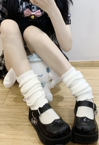 Close-up of white knitted leg warmers styled with black platform Mary Jane shoes