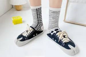 Detail of black Tabi canvas sneakers worn with striped socks on white background