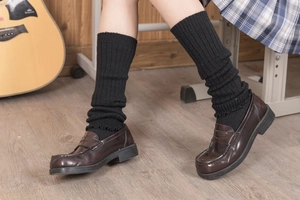 Close-up of black ribbed knit leg warmers paired with classic brown leather loafers
