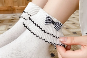Close-up of white ruffled lace ankle socks with black trim and a checkered bow detail