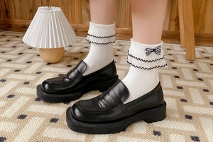 Detail of white cotton socks with black trim, lace edge, and plaid bow with leather loafers