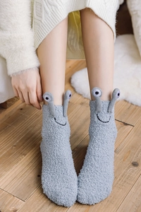 Close-up of cozy gray coral fleece socks featuring 3D snail feelers on a soft rug