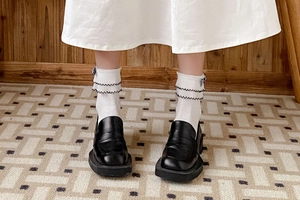 Detail of white double-layered frilly socks paired with black platform loafers shoes