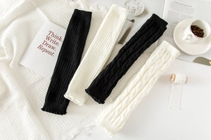 Detail of cable knit texture and ruffled cuffs on long leg warmers in black and white