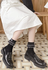 Detail of black mid-calf socks with white ruffled lace trim and striped bow accent