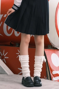 Close-up of white knit leg warmers featuring delicate ribbon bows and vertical textures