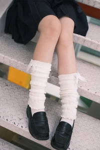 Close-up of white knitted leg warmers with silk ribbons and soft ribbed texture details
