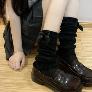 Detail of black knit leg warmer featuring a satin bow, paired with loafers and a skirt