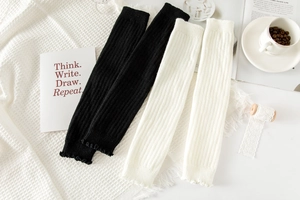 Close-up of ribbed knit leg warmers in black and white with delicate ruffled edges