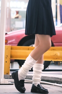 Close-up of white knitted leg warmers with cute bows paired with a black pleated skirt