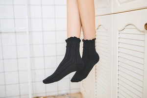 Detail of black cotton mid-calf socks with ruffled edges and vertical ribbed knit texture