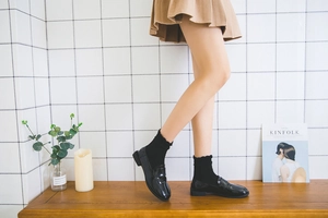 Detail of black patent leather loafers with ruffle trim socks and a brown pleated skirt